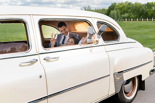 Smiling bride holding champagne near groom in retro car