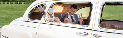 Smiling newlyweds holding champagne glasses in vintage car, banner