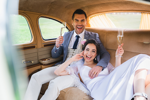 Happy newlyweds with glasses of champagne  in car