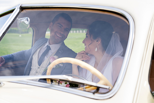 Cheerful bride and groom looking at each other in retro car