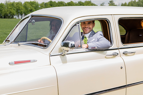 Happy groom driving vintage car near bride