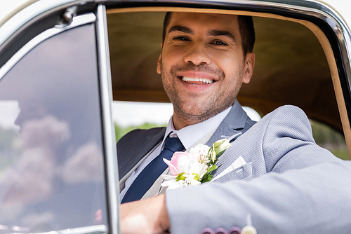 Cheerful groom in suit  near window of retro car