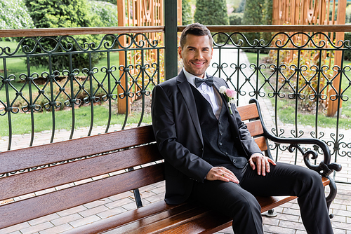 Cheerful groom in suit  on bench in patio