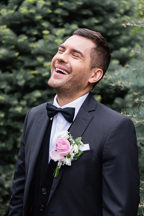 Excited groom in suit laughing in park
