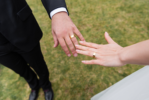 Cropped view of golden rings on hands of newlyweds outdoors