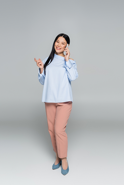 Full length of stylish asian woman talking on cellphone on grey background