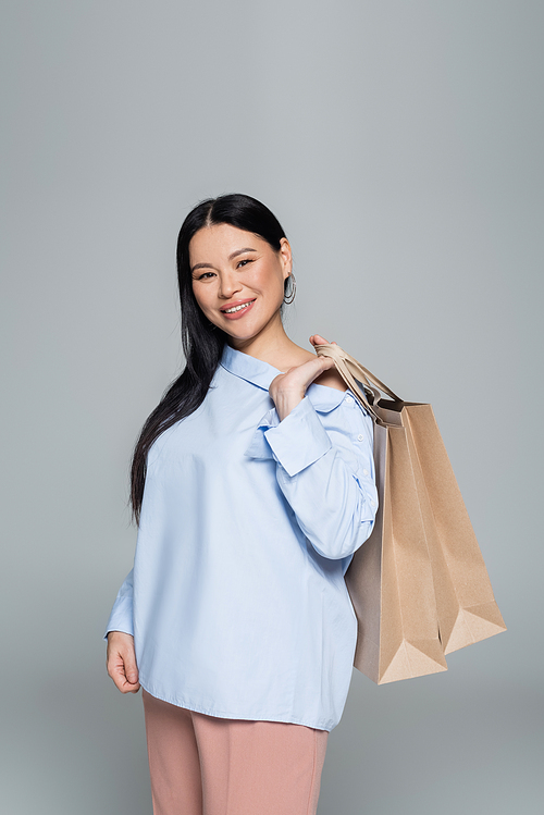 Stylish asian woman holding shopping bags and  isolated on grey