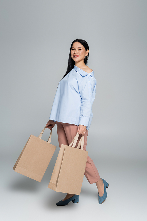 Smiling asian shopaholic holding shopping bags on grey background