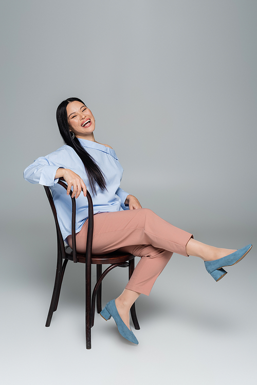 Happy and stylish asian woman posing on chair on grey background
