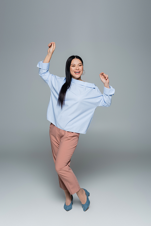 Full length of positive asian model dancing on grey background