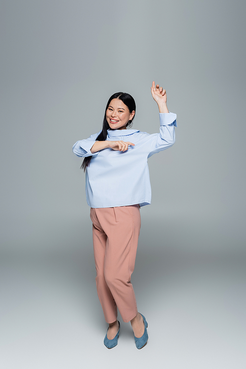Smiling asian model in blouse dancing on grey background