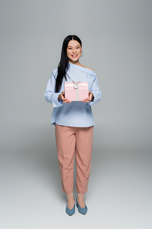 Cheerful asian model holding present on grey background