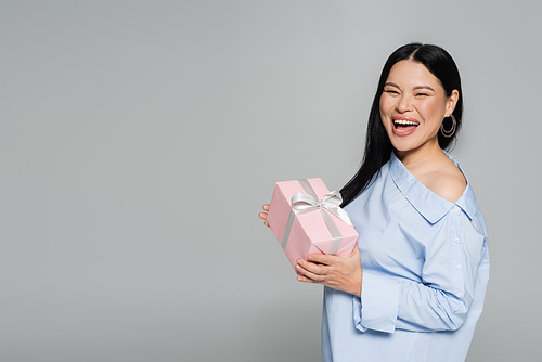 Joyful asian woman holding present isolated on grey