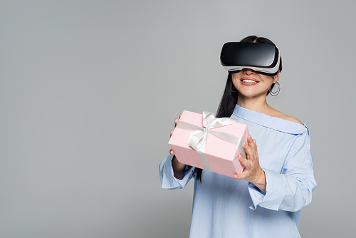 Smiling woman in vr headset holding gift isolated on grey