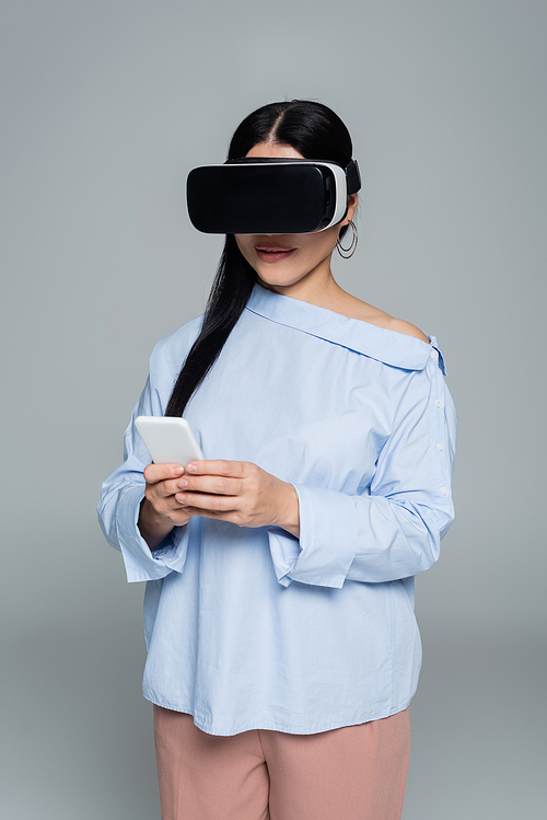 Stylish woman in vr headset using cellphone isolated on grey
