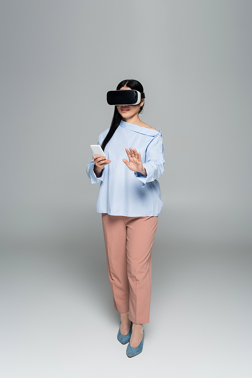 Trendy woman in vr headset using mobile phone on grey background