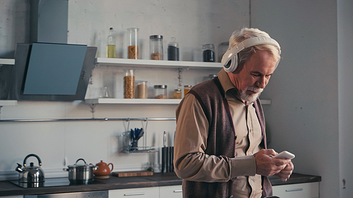bearded and senior man in wireless headphones listening music while holding cellphone