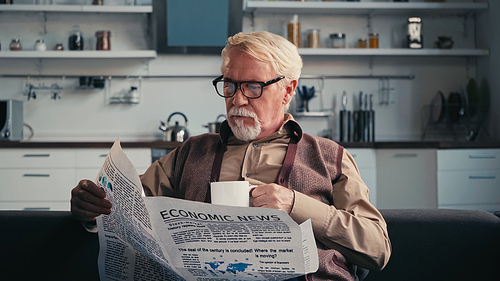 senior man in eyeglasses reading newspaper while holding cup of tea