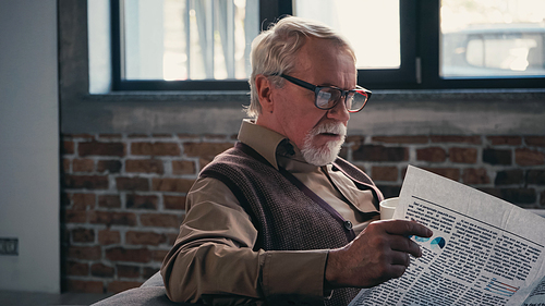 bearded senior man in eyeglasses reading newspaper at home