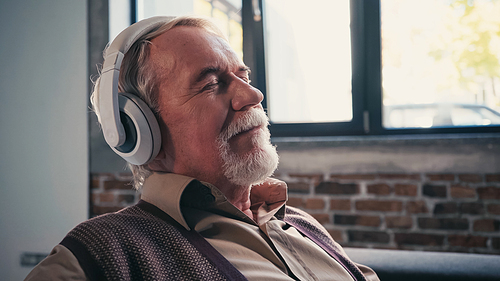 pleased senior man in wireless headphones listening music at home
