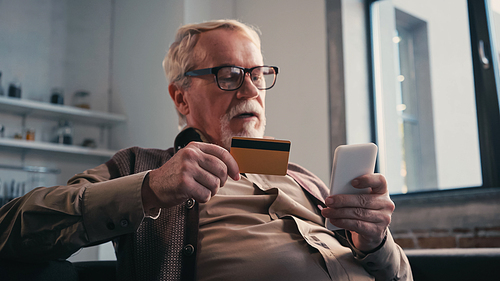 Senior man with credit card holding cellphone while shopping online at home