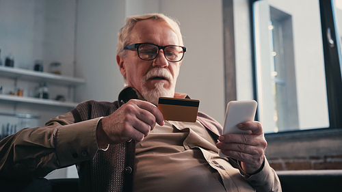 Senior man with credit card holding mobile phone while shopping online at home