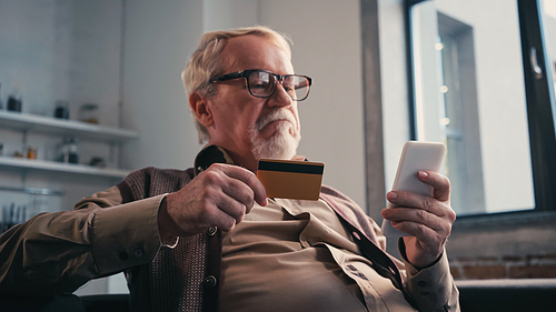 displeased senior man with credit card holding cellphone while shopping online
