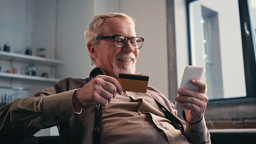 cheerful senior man with credit card holding cellphone while shopping online at home