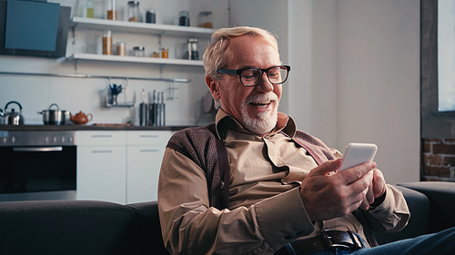 happy senior man in eyeglasses messaging on cellphone at home