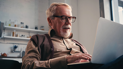 senior man in eyeglasses using laptop at home