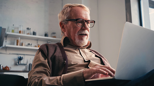 retired man in eyeglasses using laptop at home