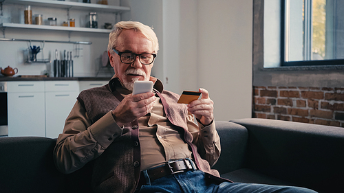 pensioner with credit card holding mobile phone while shopping online at home