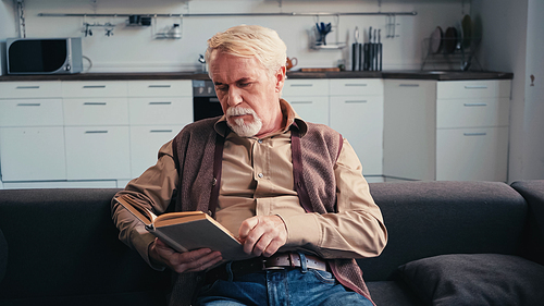 serious senior man reading book at home