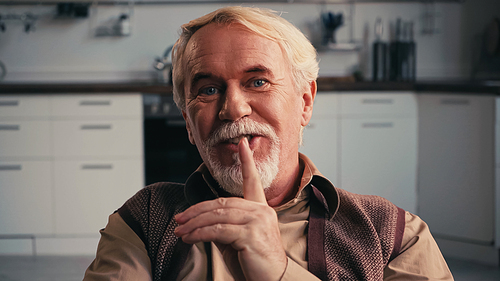 happy and bearded pensioner smiling while showing hush sign