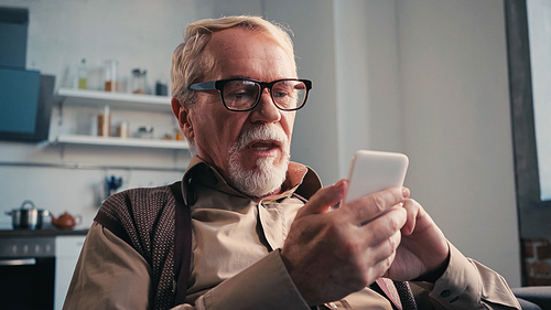 senior man in eyeglasses using smartphone