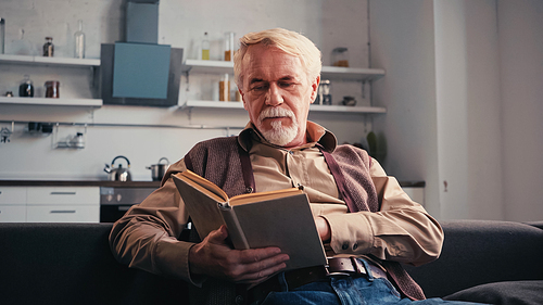 bearded retired man reading book at home