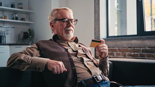 happy pensioner in eyeglasses holding credit card at home