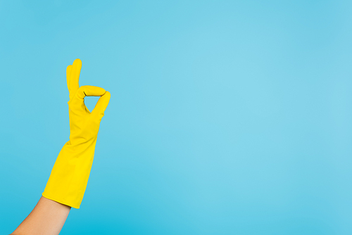 partial view of housewife in yellow rubber glove showing okay gesture isolated on blue