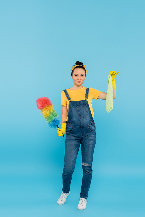 full length view of housewife with colorful dust brush and rag  on blue