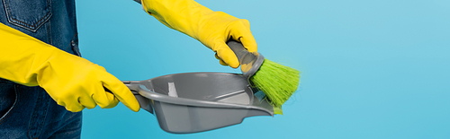 cropped view of woman in yellow rubber gloves holding scoop and broom isolated on blue, banner