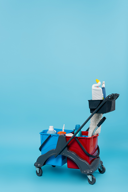 cart with different cleaning supplies and buckets on blue background