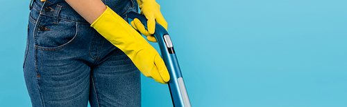 cropped view of housewife in yellow rubber gloves using vacuum cleaner isolated on blue, banner