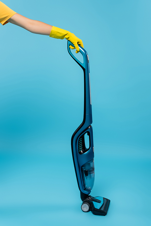 cropped view of housewife in yellow rubber glove holding modern vacuum cleaner on blue