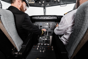 bearded pilot in cap using thrust lever near co-pilot in airplane simulator