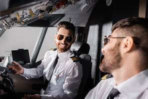 cheerful pilots in sunglasses looking at each other in airplane