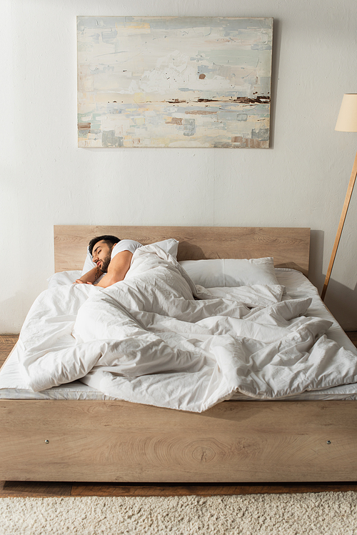 Young bearded man sleeping on white bedding at home