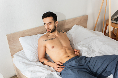 Shirtless bearded man lying on bed in morning