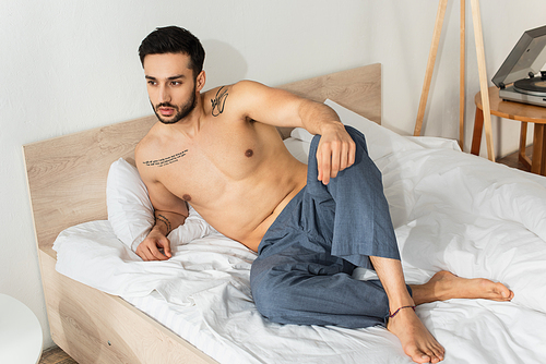 Shirtless tattooed man looking away on bed in morning