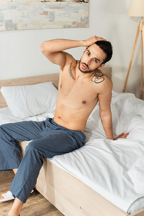 Shirtless man in pants  while sitting on bed