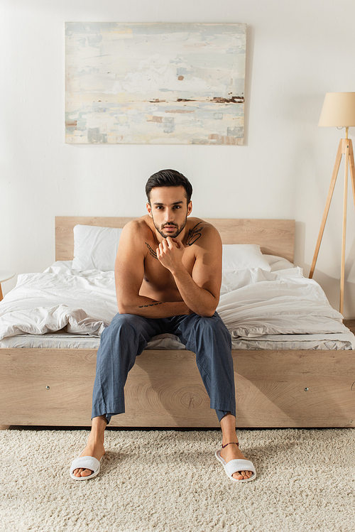 Shirtless man in slippers and pants  on bed